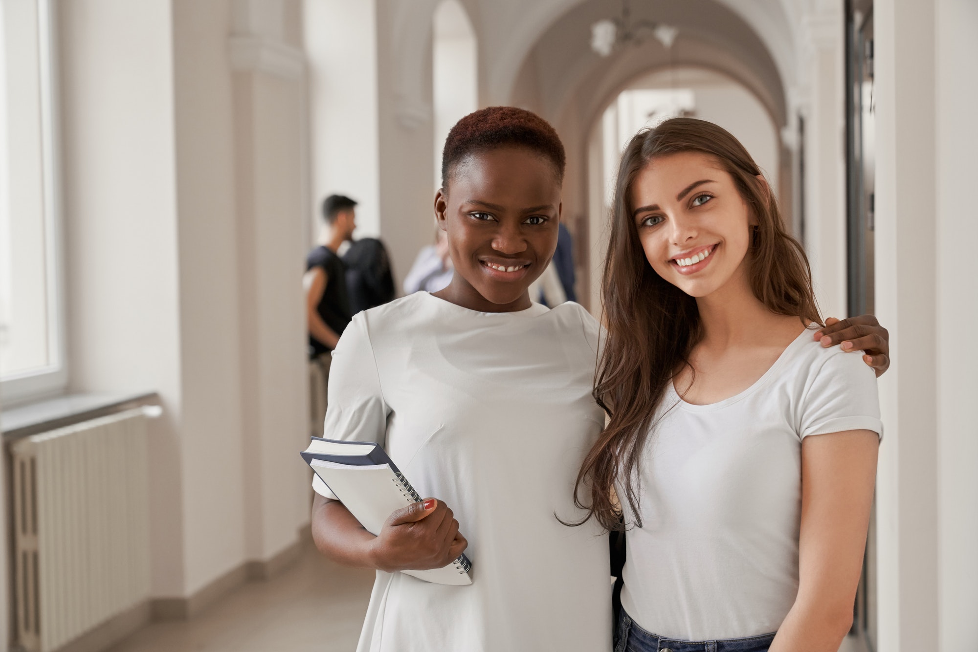 Female students African and Caucasian embracing